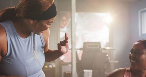 Backlit Black Women Chatting and Laughing in Activewear by Treadmill, Fitness Friendship