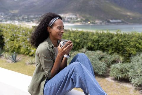 Young woman relaxing with coffee on coastal terrace overlooking bay and mountains