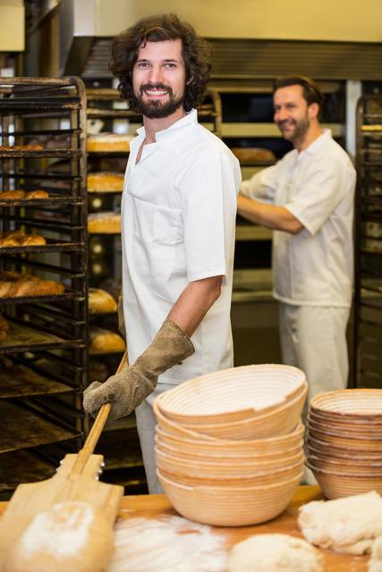 Portrait of two smiling bakers preparing bread in bakery kitchen