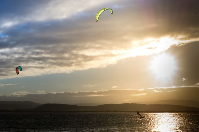 Powerful image capturing the thrill of kiteboarding during an enchanting sunset on water. Highlights colorful kites against dramatic sky and serene water landscape. Perfect for promoting water sports, travel, adventure to nature enthusiasts, or websites related to extreme activities and outdoor recreation.