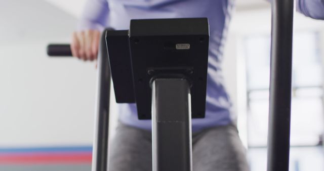 Close-up view of individual working out on elliptical trainer in a gym. Useful for illustrating fitness routines, cardio workouts, healthy living, and sports equipment in indoor settings.