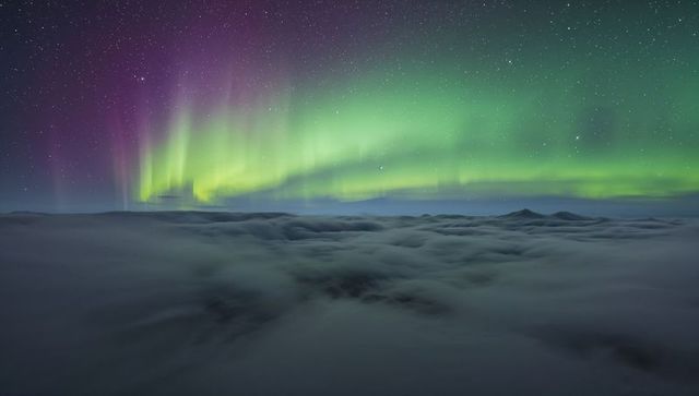 Dancing Aurora Borealis Curtains in Emerald and Violet Over Mountain Cloud Deck