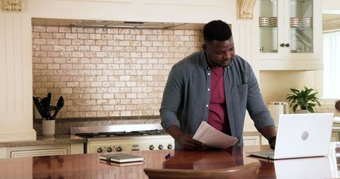 Man working on budget plans in home kitchen with laptop