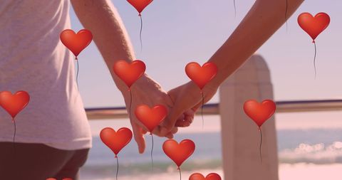 Romantic Couple Holding Hands with Heart Balloons at Seaside