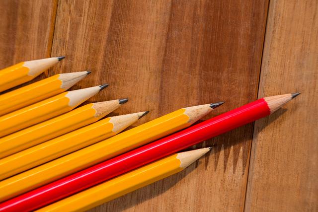 Close-up view of several yellow pencils and one red pencil arranged on a wooden table. Ideal for use in educational materials, office supply advertisements, creative projects, and back-to-school promotions.