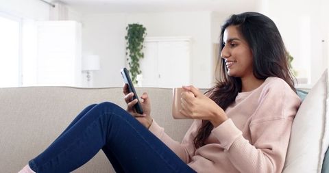 Woman Relaxing on Sofa with Smartphone and Coffee Mug at Home