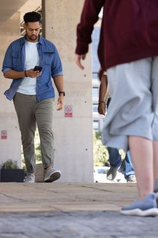 African american commuter walking while using smartphone under urban concrete pillars