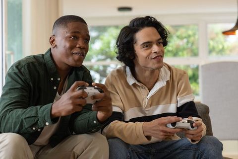 Friends playing video games on couch holding white controllers in bright living room