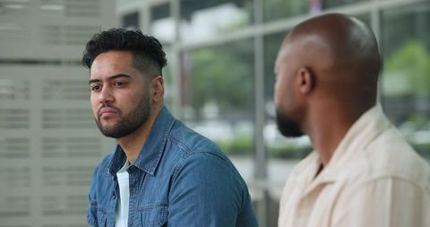 Diverse men talking at bus shelter waiting for transit, urban casual conversation