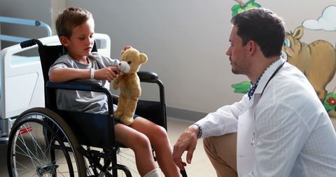Caring doctor with child patient in wheelchair at hospital