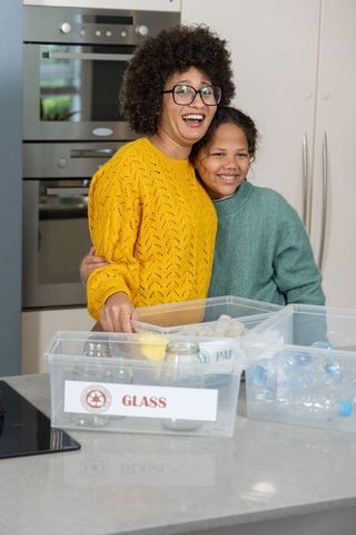 African american mother and daughter sorting glass recycling in bright modern kitchen