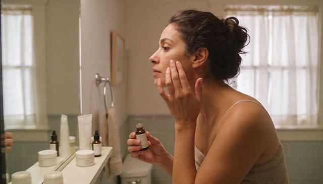 Applying facial serum at vanity in towel morning skincare routine
