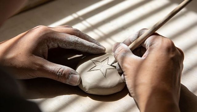 Artisan hands carving star into soft clay disc with sunlit shadow lines, close-up pottery