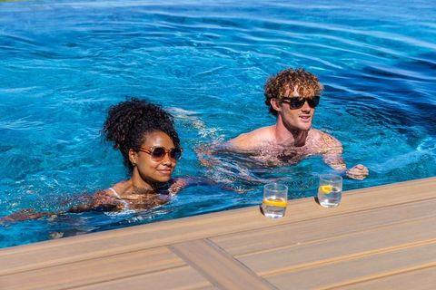 Diverse couple relaxing in resort pool on luxury deck with lemon drinks
