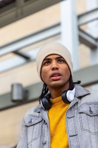 Young african american man wearing beanie and headphones looking up under urban canopy