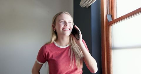Teen Girl Talking on Smartphone by Window Smiling Happily