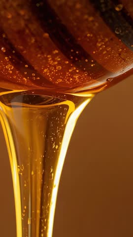 Tilting honey dipper releasing golden honey ribbon in slow-motion vertical video
