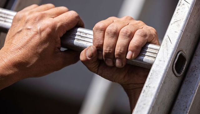 Weathered hands gripping aluminum ladder rung showing strength and manual labor details