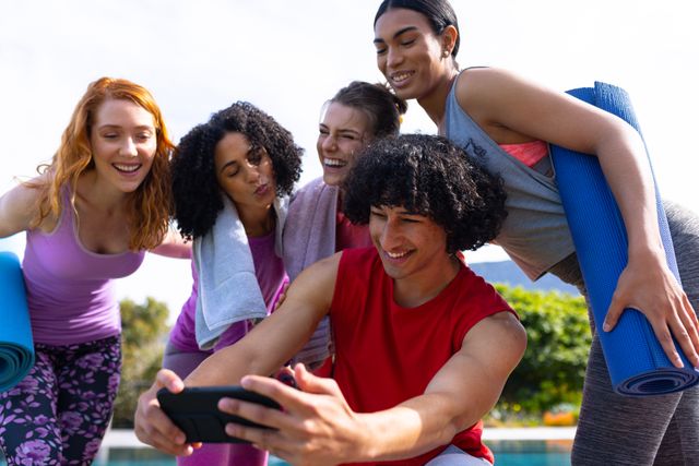This image shows a diverse group of friends taking a selfie after a yoga session in a sunny garden. They are holding yoga mats and smiling, capturing a moment of togetherness and happiness. Ideal for promoting fitness, healthy lifestyles, social activities, and community bonding.