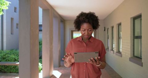 Woman using tablet in sunlit campus colonnade for remote work, study and professional focus