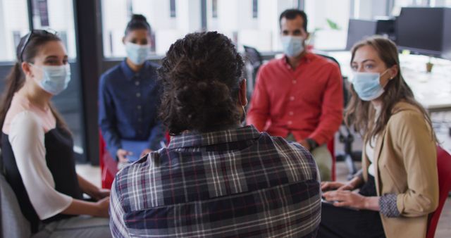Diverse group of business colleagues wearing face masks discussing. working at the office of an independent creative business during covid 19 coronavirus pandemic.