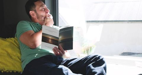 Man Contemplating Next to Window with Book in Hand