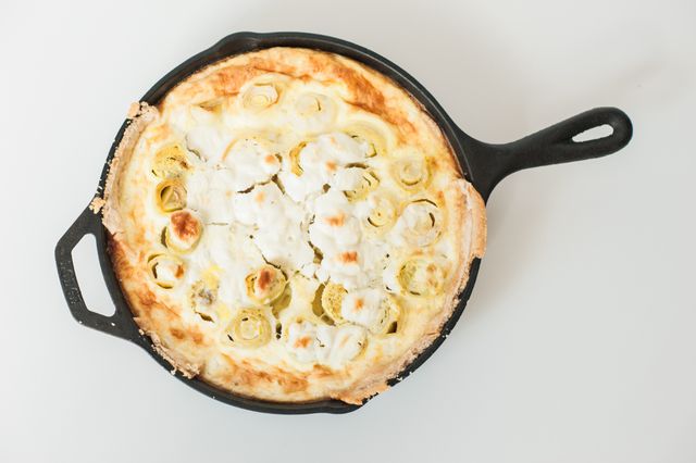 Overhead view of a freshly baked leek and cheese quiche in a cast iron skillet on light background. Ideal for food blogs, cooking websites, recipe illustrations, and culinary magazines. Perfect for showcasing comfort food, vegetarian recipes, and DIY cooking enthusiasts.