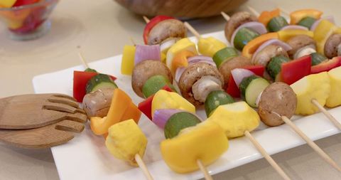 Colorful vegetable skewers on white plate with wooden tongs