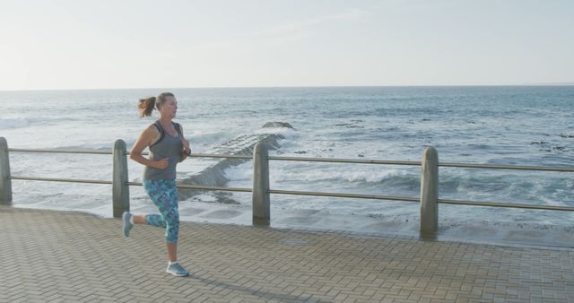 Woman jogging along an ocean promenade in the morning light, enjoying a healthy and active lifestyle. Ideal for wellness, fitness, and outdoor activity promotions, or articles related to health and exercise.