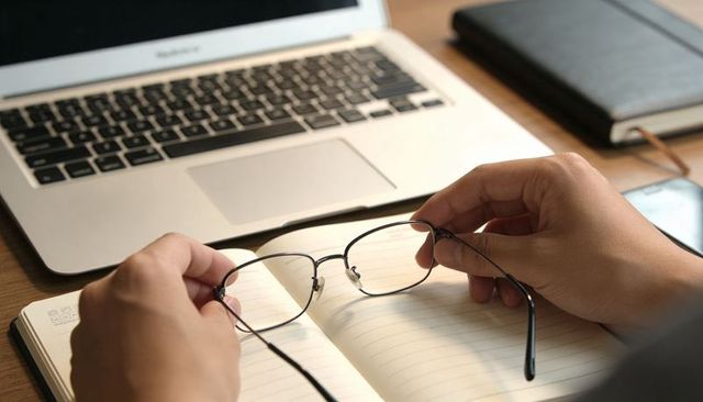 Holding metal glasses over open notebook at laptop workspace, home office routine
