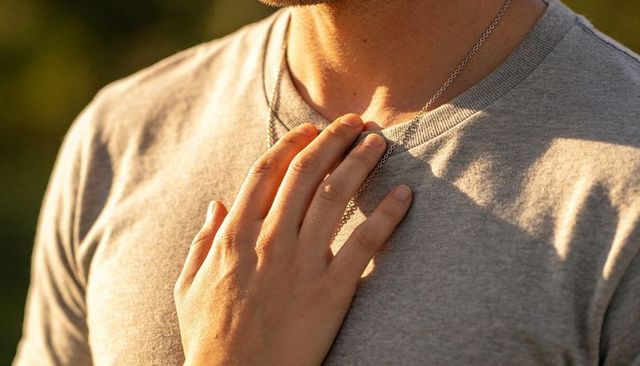 Hand resting on male chest wearing silver chain and gray t-shirt in golden hour light