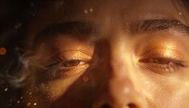 Golden glam closeup: metallic gold eyeshadow on relaxed woman with glitter, bokeh