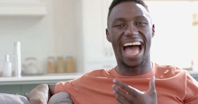 Smiling African American man laughing in a bright kitchen. He is enjoying relaxed moment at home. Perfect for promoting positive lifestyle, casual home settings, or happiness-related content.