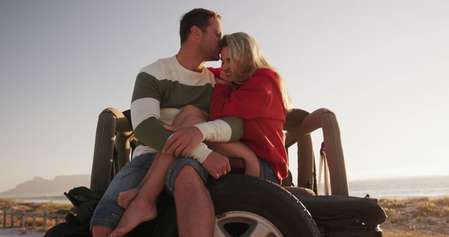 Man and woman share intimate moment on off-road vehicle with scenic beach backdrop at sunset. Ideal use for travel promotions, romantic vacation advertisements, relationship-focused content, or scenic outdoor lifestyle imagery.