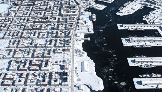 Aerial winter harbor showing snow-covered urban grid, icy piers, ships and ice floes