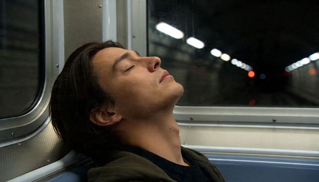 Young man resting on subway bench closing eyes leaning back by window with tunnel lights