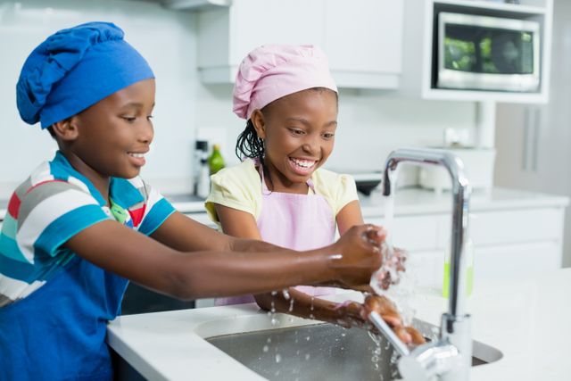 Smiling siblings washing hand in kitchen at home