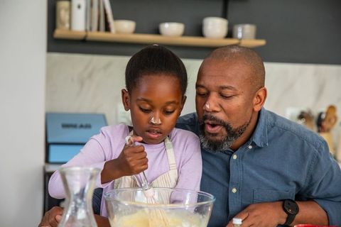 African american father teaching daughter baking while mixing batter in kitchen