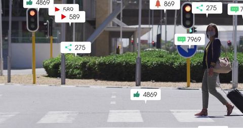 Masked commuter crossing urban zebra crosswalk pulling luggage with social notifications