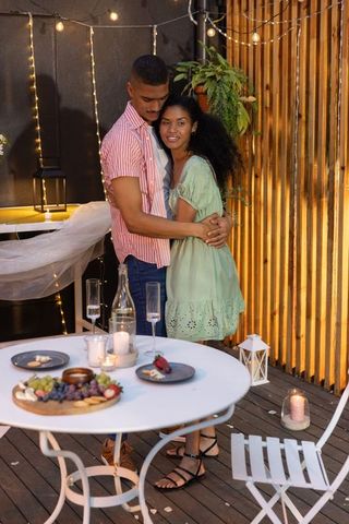 Young couple embracing on candlelit wooden deck, enjoying romantic outdoor evening dinner