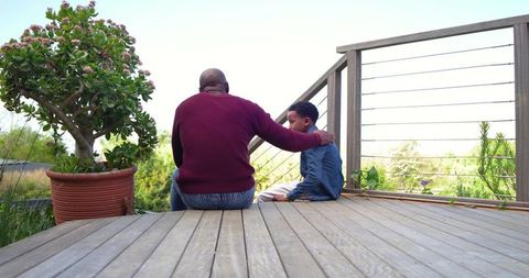 African american father comforting son on wooden deck overlooking garden family bonding