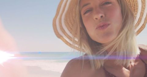 Blonde Woman in Sun Hat Blowing Kiss on Sunny Beach Day