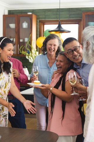 Multi-generational friends celebrating birthday in kitchen with cupcake, wine and laughter