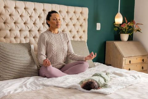 Mother meditating on bed while baby resting on plush blanket for calm mindful parenting