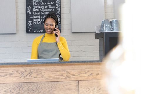 African american barista smiling while taking phone order and processing payment at coffee counter