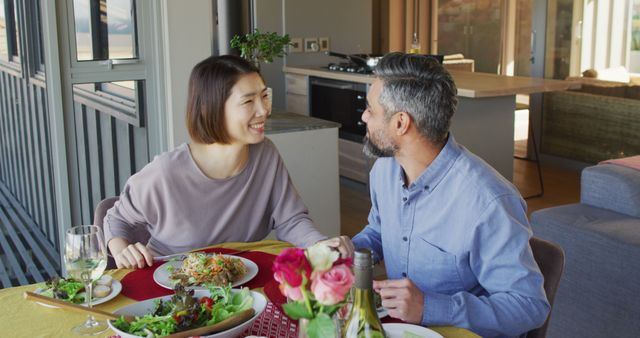 Couple having lunch together at home in a cozy dining area. Bright flowers on the table create a pleasant atmosphere. Perfect for illustrating concepts related to family bonding, healthy meals, indoor lifestyle, and intimate moments.