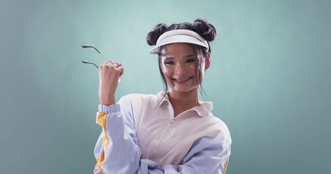 Young Asian woman smiling and posing with visor and sunglasses in pastel fashion portrait mint style