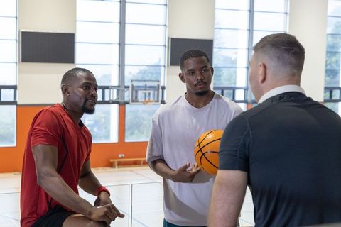Coach leading strategy huddle with diverse male basketball players holding ball on court