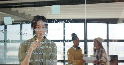 Creative Female Professional Working on Transparent Whiteboard in Office