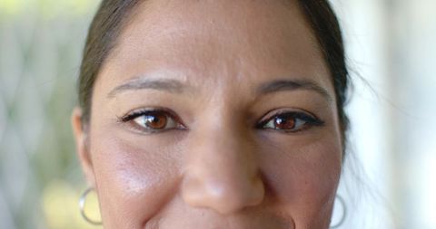 Closeup smiling woman wearing eyeliner and silver hoop earrings on sunlit porch